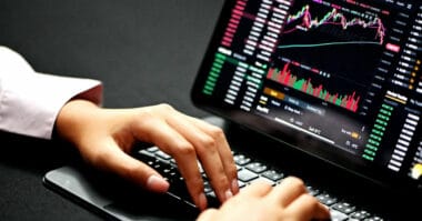 Person scalping stocks online, analyzing financial charts on a laptop in a dimly lit room.